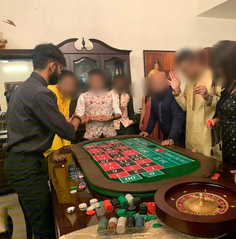 Guests around a roulette table with a dealer at a house party